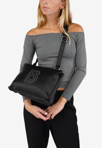 Bolso cruzado de cuero negro con una superficie texturada y detalle de logo con tachuelas. Cuenta con una correa ajustable y cierre con cremallera.