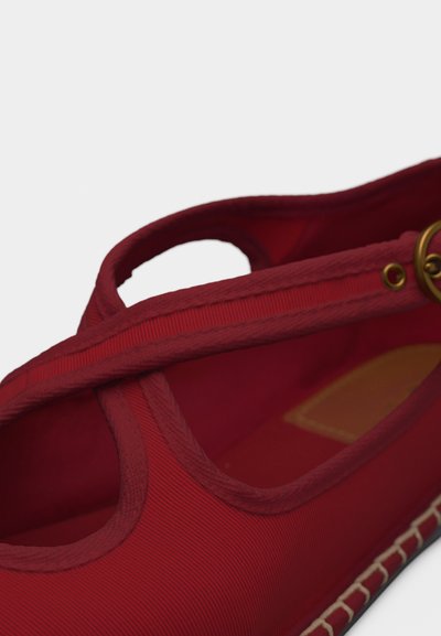 Κόκκινο ύφασμα παπούτσι Mary Jane με στρογγυλό χρυσό αγκράφα και ορατή ραφή κατά μήκος της σόλας, σε κοντινή γωνιακή κορυφαία άποψη.