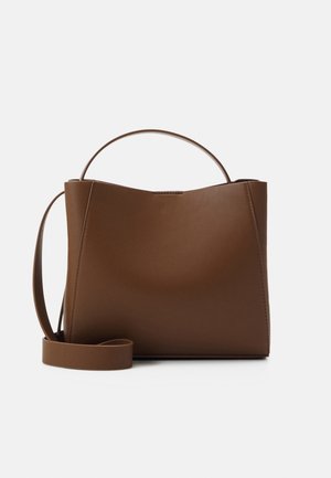 Sac à main en cuir marron avec une poignée incurvée et une bandoulière amovible, posé debout sur une surface blanche.