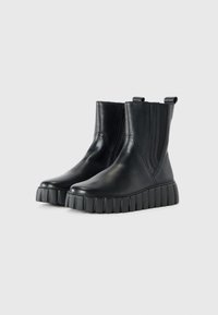 Botas de cuero negras hasta el tobillo con paneles laterales elásticos y suelas de goma gruesas con un diseño estriado. Textura suave, diseño minimalista.