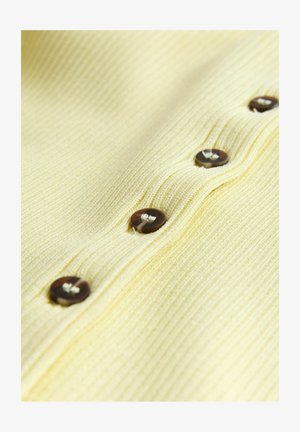 Close-up of a pale yellow ribbed fabric with a row of dark brown buttons sewn in a vertical line.