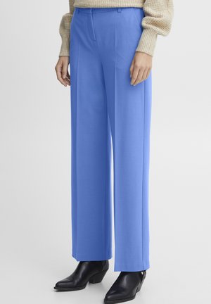 Lichtblauwe wijdvallende broek met een platte voorkant, gemaakt van een gladde stof. Gecombineerd met zwarte enkellaarzen, die een schoon ontwerp laten zien.