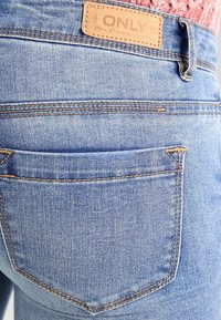 Vaqueros de denim azul claro con costuras marrones, que cuentan con una etiqueta de cuero con "ONLY" en la cinturilla y un diseño de bolsillo trasero.