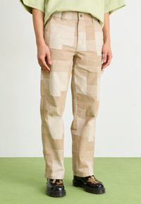 Beige mønstrede cargo bukser med store, lyse kvadratisk lapper, præget af en lige pasform og en forknaplukning, båret med sorte støvler.