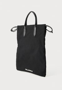 Czarna torba na ramię z kanwy z czarnymi skórzanymi uchwytami, charakteryzująca się prostym designem, miękką teksturą i białym logo "KARL LAGERFELD" na dole.