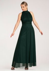 Ciemnozielona maxi sukienka z wysokim dekoltem, plisowanym topem i przezroczystą warstwą spódnicy. Wykończona dopasowaną talią i subtelnymi bocznymi rozcięciami.