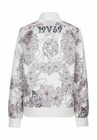 Vit bomberjacka med pastellfärgade blommor och lejon grafisk design. Har ribbade mudd och nederkant, med "1969" tryckt på övre ryggen.