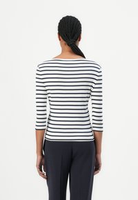 Gestreiftes langärmliges Oberteil in Weiß und Marineblau mit einem Bootsausschnitt und passgenauer Silhouette, kombiniert mit dunklen Hosen. Glatte Stoffstruktur.