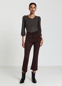 Maglione nero lavorato a maglia con design a treccia, abbinato a jeans a vita alta marroni a campana con orli grezzi. Stivaletti neri alla caviglia completano il look.