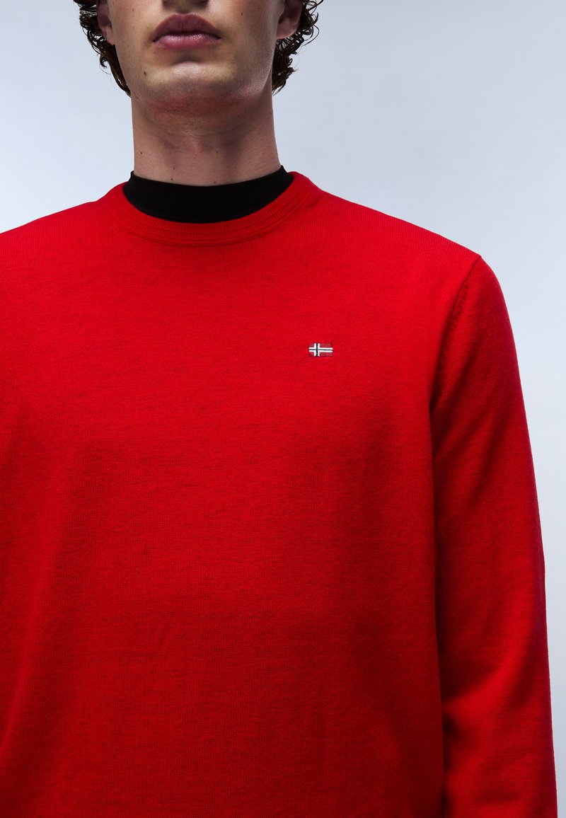 Czerwony sweter dzianinowy z okrągłym dekoltem i prążkowanymi mankietami. Posiada małe logo na piersi, prezentując gładką teksturę i klasyczny krój.