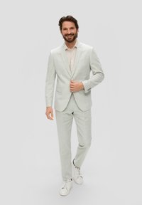 Lichtgrijs, gestructureerd pak gecombineerd met een licht shirt en witte sneakers; heeft een getailleerde blazer en recht gesneden broek.