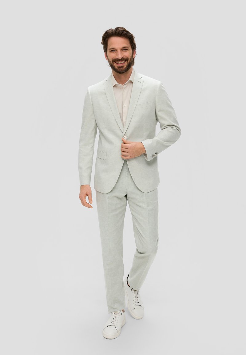 Lichtgrijs, gestructureerd pak gecombineerd met een licht shirt en witte sneakers; heeft een getailleerde blazer en recht gesneden broek.
