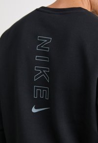 Sort sweatshirt med et vertikalt "NIKE" logo i lysegrå på bagsiden, rund halsudskæring og blød tekstur.