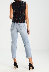 Svart rutig ärmlös topp med fransiga kanter, kombinerad med ljusblå högmidjade jeans med råa kant och bakfickor. Svarta högklackade skor.