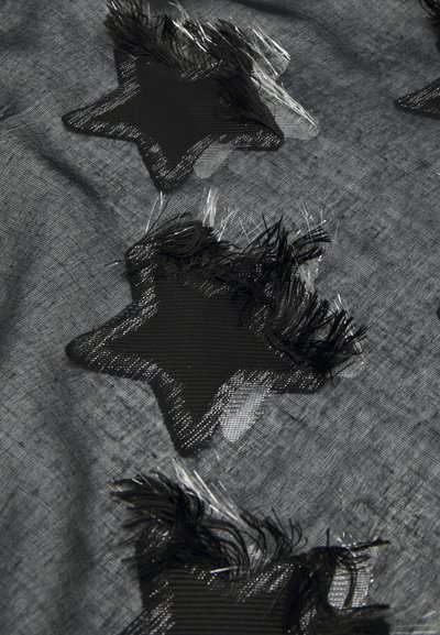 Applicazioni a forma di stella nera con dettagli frangiati sono cucite su uno sfondo di tessuto grigio trasparente e testurizzato, creando un design a strati.