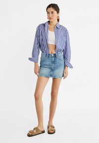 Prúhovaná modro-biela prevelká košeľa, priliehavý biely crop top, svetlomodrá denimová minisukňa a hnedé sandále s prackami.