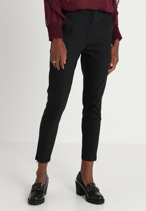 Pantalon noir slim-fit jusqu'à la cheville porté avec des mocassins noirs à talons blocs et un chemisier bordeaux à manches longues avec poignets froncés.