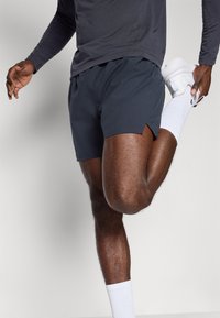 Dark gray athletic shorts with slits at the sides, paired with white athletic socks and shoes; smooth fabric, fitted design.