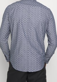 Námořnická košile s dlouhými rukávy a geometrickým bílým vzorem, s tradičním límcem a zapínáním na knoflíky, vyrobená z lehkého materiálu.