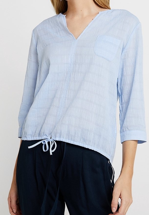 Helles blaues, strukturiertes Oberteil mit V-Ausschnitt, Dreiviertelärmeln und einer Brusttasche. Verfügt über einen Kordelzugsaum für eine verstellbare Passform.