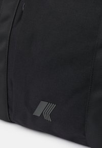 Sac de sport en tissu noir avec une surface texturée et un logo noir brillant à rayures superposées sur un côté.