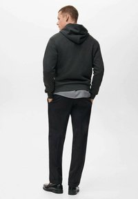 Donkergrijze hoodie met een gestructureerde stof en een capuchon, gecombineerd met zwarte broek en zwarte schoenen, gezien vanaf de achterkant.