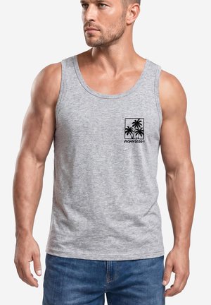 Muskelbepackter Mann trägt ein hellgraues Tanktop mit schwarzem Palmen-Design und Schriftzug auf der linken Brustseite, kombiniert mit blauen Jeans.
