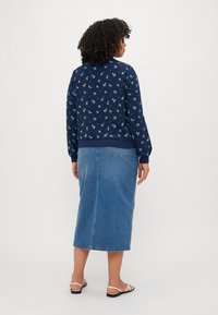 Sweatshirt en fleur marine avec des poignets côtelés, associé à une jupe en denim de longueur mi-jambe. La jupe présente une couture arrière et deux poches arrière.