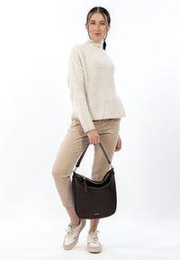 Ruskea nahkainen käsilaukku, jossa on kaareva muoto, vetoketjusuljenta ja lyhyt musta hihna. Yhdistetty vaaleankermanväriseen ribbineulepaitaan ja beigenvärisiin housuihin.