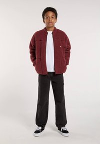 Burgundia fliisjope kõrge kaelusega, kahe esitaskuga, kombineeritud mustade pükste ja mustade tossudega. Valge T-särk all.