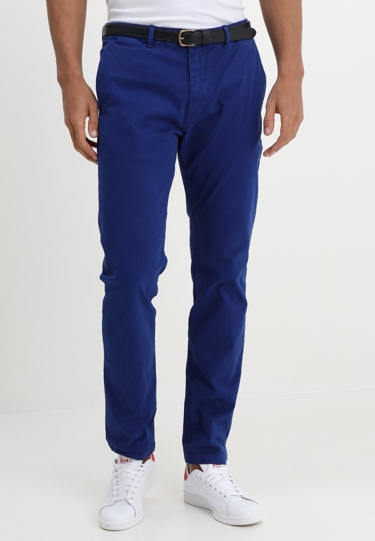 Slim-fit, blauwe katoenen chino's met steekzakken aan de voorkant, een ritssluiting en een zwarte riem. Gecombineerd met witte sneakers en een aansluitend wit topje.
