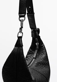 Schwarze Ledertasche mit strukturierter Oberfläche, ausgestattet mit einem Reißverschluss und verstellbarem Riemen mit Metallbeschlägen.