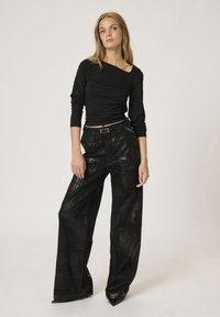 Zwarte longsleeve top met gathered details, gecombineerd met hoge taille, wijde zwarte broek met een textuurpatroon en glanzende afwerking.