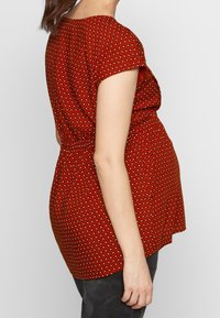 Rød mønstret top med korte ærmer og elastisk talje. Har et geometrisk print i hvid og sort, designet til en løs pasform.