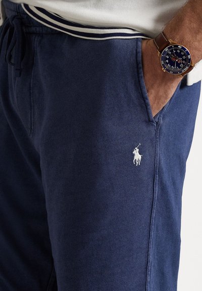 Pantalons de survêtement bleu marine avec un cordon de serrage à la taille, dotés d'un petit logo brodé blanc sur la poche gauche. Tissu en coton doux.