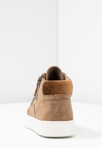 Chaussure montante en daim marron avec une semelle extérieure blanche, dotée d'un talon texturé, d'une fermeture éclair latérale et d'un accent en toile à l'arrière.