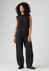 Zwarte mouwloze top gecombineerd met losvallende zwarte denim jeans. De outfit heeft een eenvoudig ontwerp en een zachte textuur. Zwarte enkellaarsjes maken de look compleet.