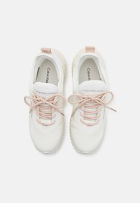 Hvite joggesko med en glatt syntetisk overdel, rosa snøring og teksturerte såler med en lysfarget aksent. Merkenavnet er synlig innvendig.