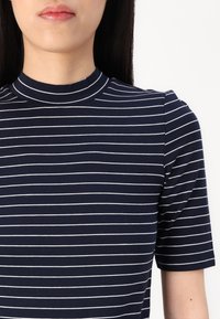 Tricou bleu marin cu dungi, cu mâneci scurte și guler înalt; are dungi albe orizontale și o textură de țesătură netedă.