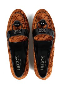 Para z teksturowanych, spalonych pomarańczowych loafersów z czarnymi lakierowanymi paskami i dużymi czarnymi ozdobnymi koralikami na górze, oznaczone Hego's Milano.