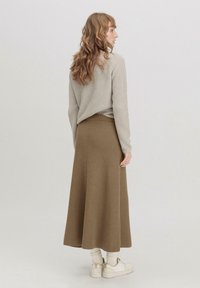 Rippstrick, langärmeliges beiges Oberteil kombiniert mit einem braunen Rippstrick-Maxikleid. Weiße knöchelhoche Turnschuhe vervollständigen das Outfit.