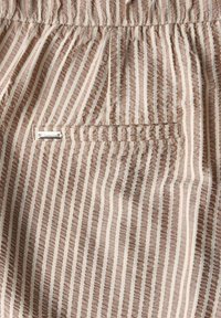 Beige och vit vertikalt randig tyg med en elastisk midjeband och en liten rektangulär sydd bakficka.