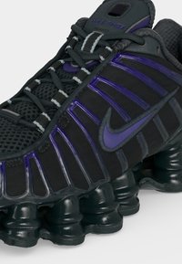 Μαύρο και μοβ αθλητικό παπούτσι Nike Shox με μαξιλαρωμένη σόλα, πλεκτό επάνω μέρος και εμφανές λογότυπο Nike στη πλευρά.