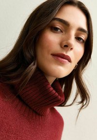 Pull en col roulé côtelé bordeaux avec une texture douce. Vue rapprochée mettant en valeur une coupe décontractée et les traits du visage du modèle.