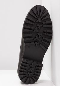 Semelle de chaussure noire avec un motif de crampons profonds comprenant des formes triangulaires et rectangulaires, conçue pour l'adhérence et la durabilité. Taille indiquée 37.
