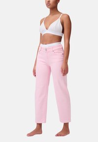 Jeans in denim rosa con taglio dritto e vita alta, dotati di chiusura frontale con bottone e passanti per cintura. Abbinati a un bralette bianco.