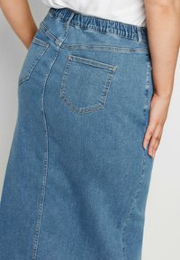 Denimhame, jossa on joustava vyötärö, suora malli, kaksi takataskua ja haalistunut sininen pesu, jossa on näkyviä ompeluyksityiskohtia.