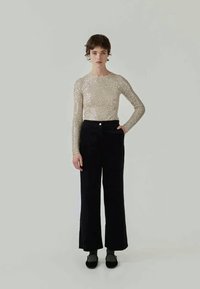 Haut à manches longues, ajusté, en or métallisé avec une finition texturée et scintillante, associé à un pantalon noir à jambes larges et des chaussures plates noires.