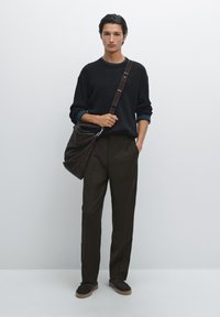 Schwarzer strukturierter Strickpullover, braune Hose, dunkelbraune Schultertasche und braune Schuhe mit Gummisohle, vor einem schlichten weißen Hintergrund.
