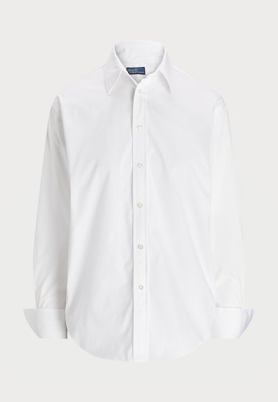 Camisa blanca de manga larga hecha de algodón, con cuello tipo polo, botones en la parte delantera y dobladillo redondeado. Textura suave, diseño clásico.
